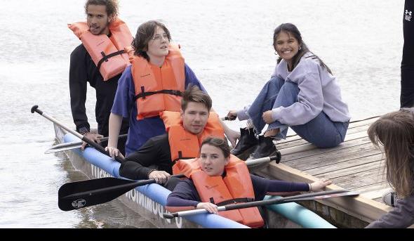 One woman on a pier next to three people in a canoe. 