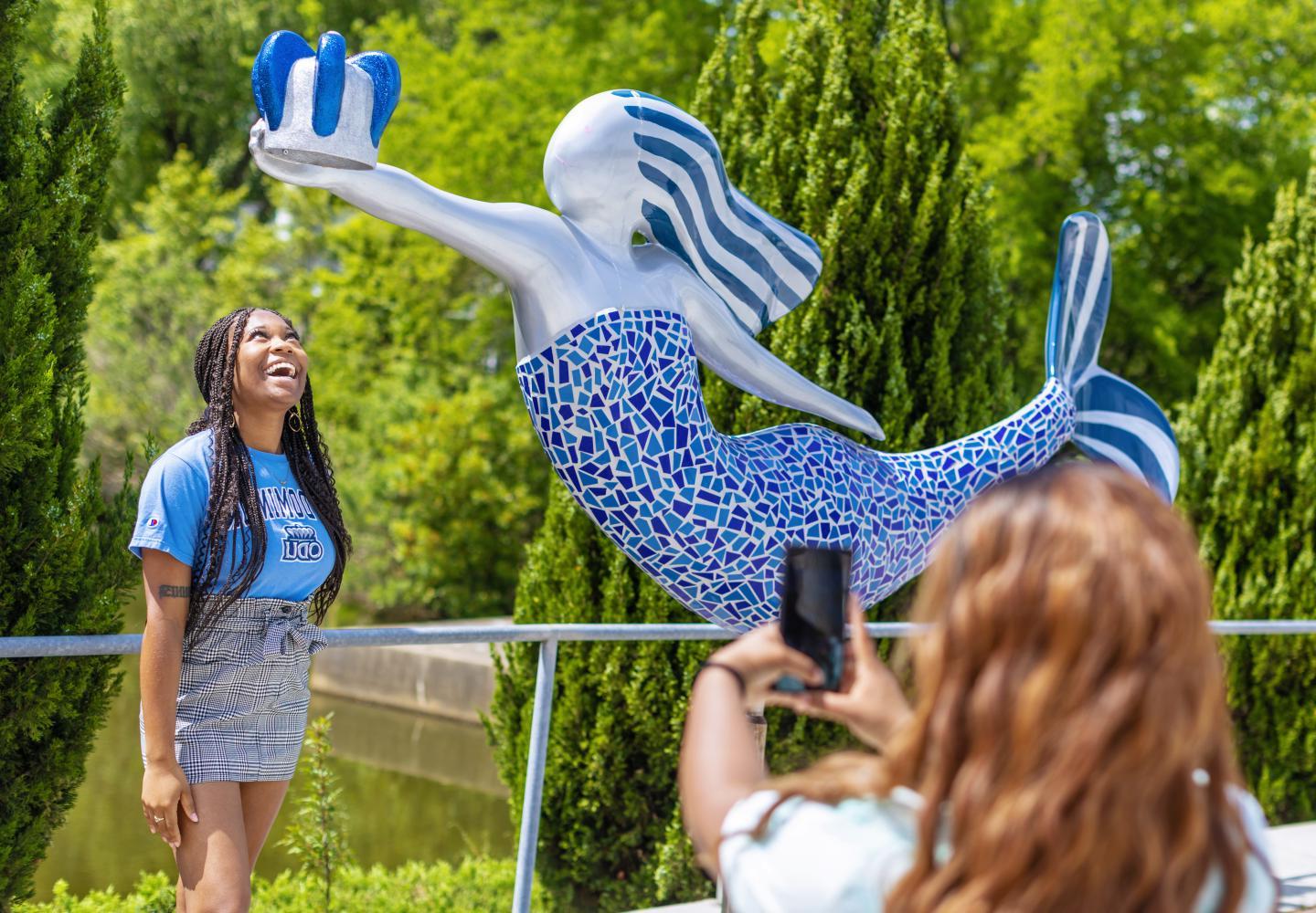 A female ODU students stands underneath reign the mermaid stature