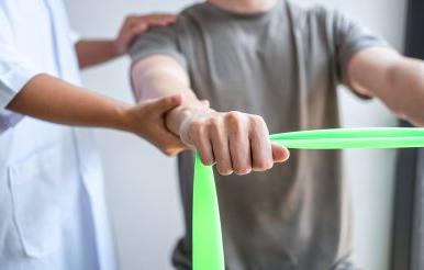 Physical Therapist helps male patient use resistance band