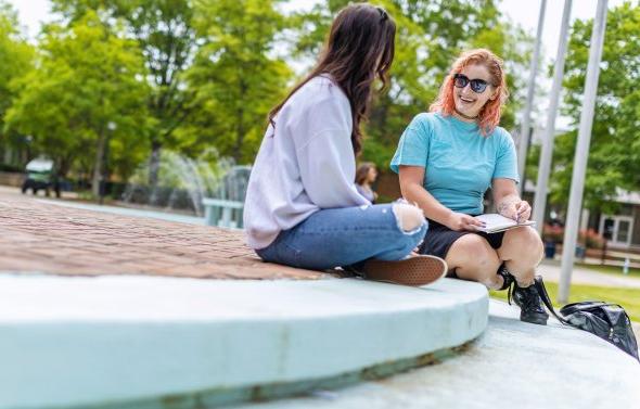 Two female students are sitting on the steps in front of the Webb center talking