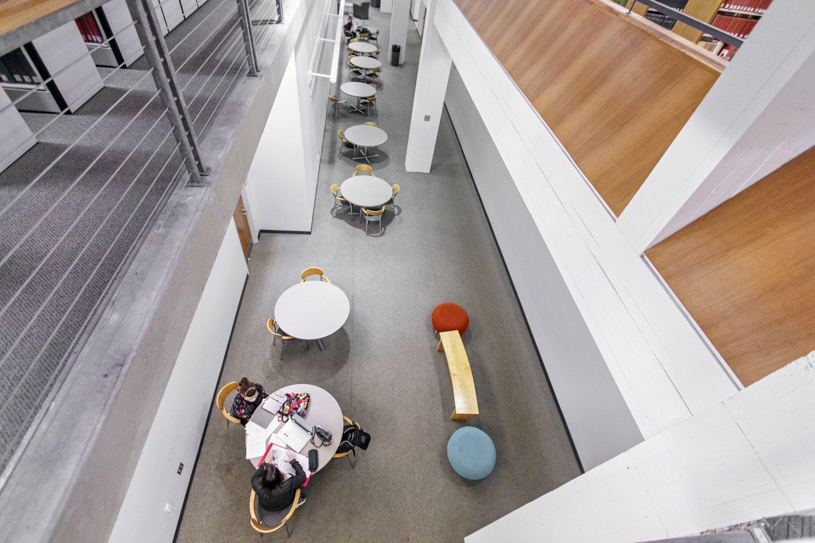 Desks in a library with students studying as viewed from the second floor.